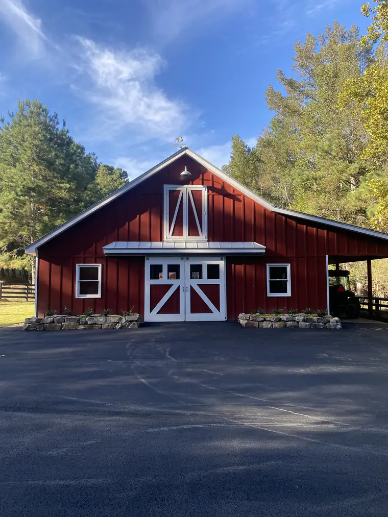 Fresh asphalt parking apron in front of a red board-and-batten barn with white doors and stone planters