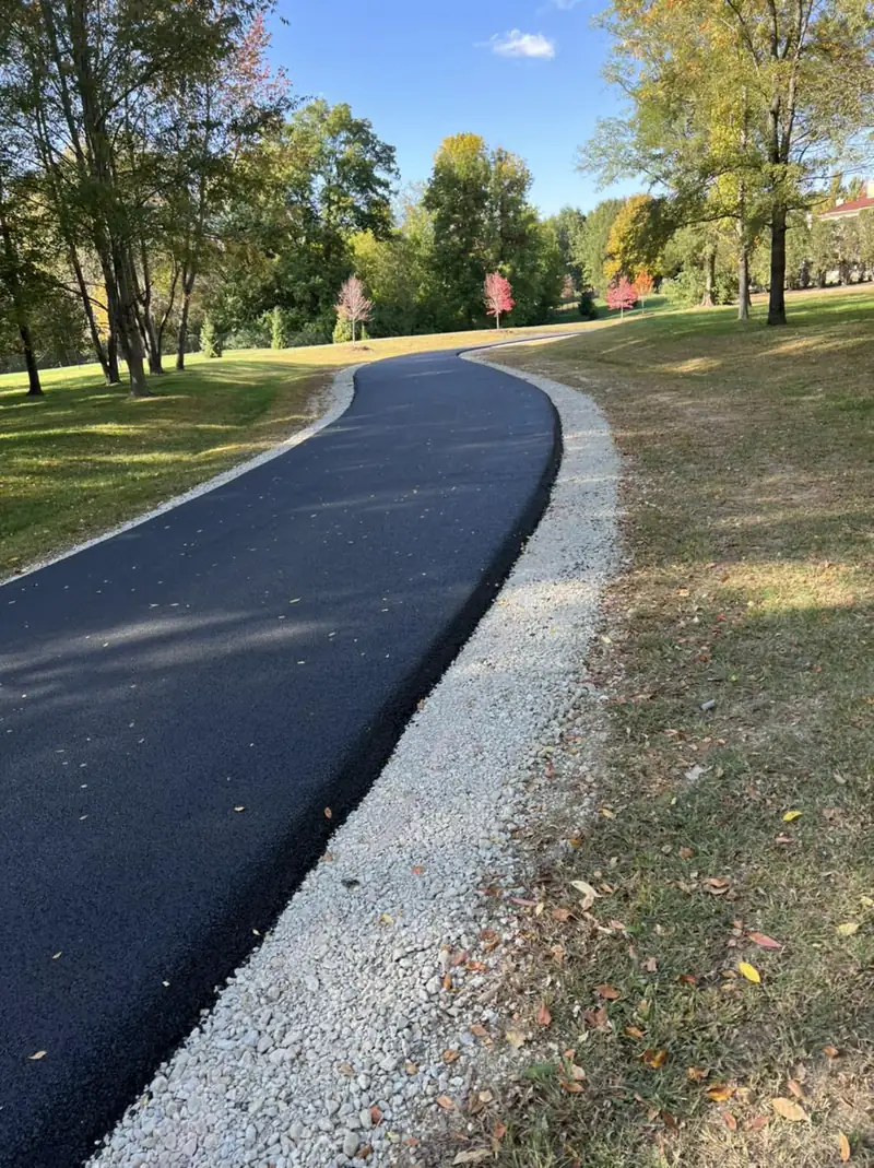 Freshly paved asphalt drive curving through a park-like lawn with crushed limestone shoulders and fall-colored maples