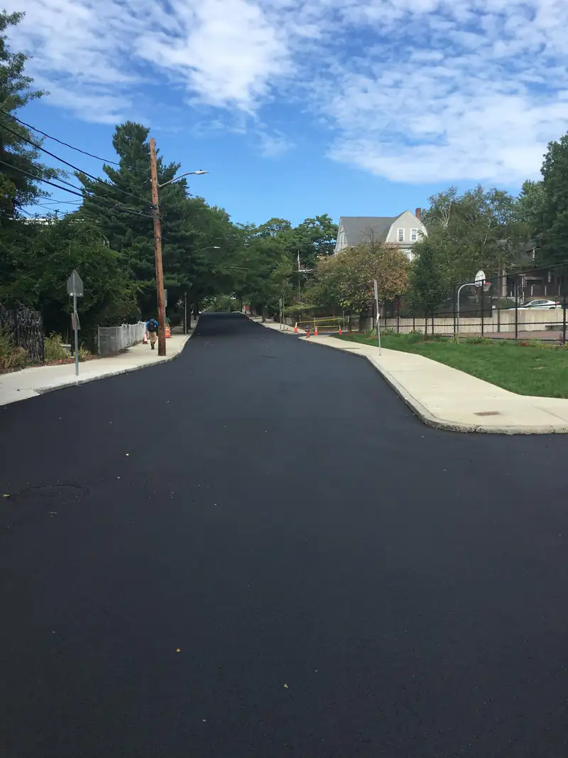 Freshly resurfaced residential street with new black asphalt, concrete sidewalks and mature shade trees on a sunny day