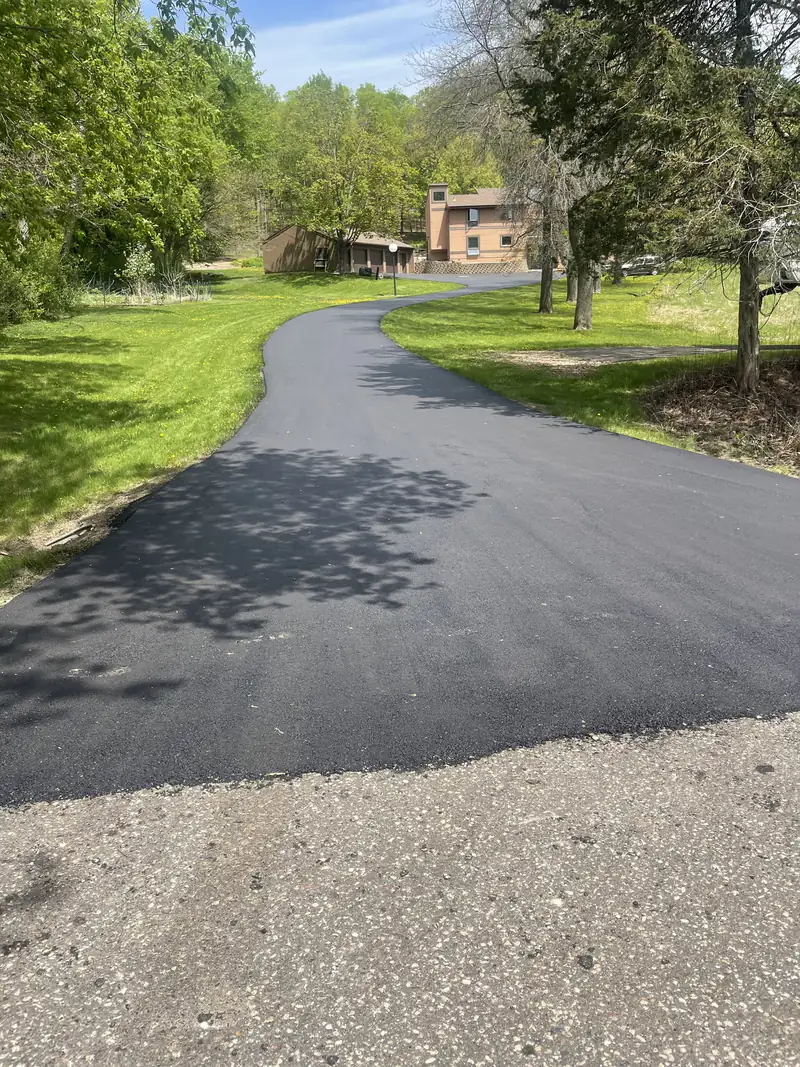 Smooth new asphalt driveway winding up a wooded hillside to a cedar-sided home and detached garage